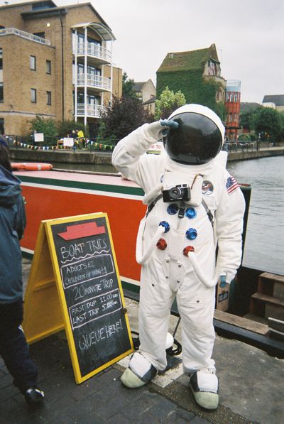 A man in a space suit stands beside a boat, saluting