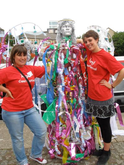 Two red-shirted volunteers with a character whose costume defies description