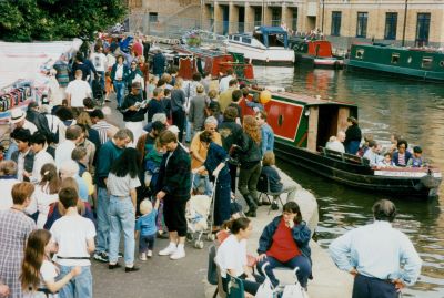 Stalls left and crowds centre on the towpath, boats to the right