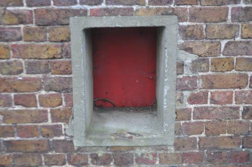 A square red door recessed in a thick brick wall