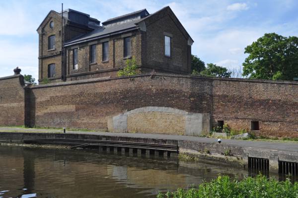 A large imposing building behind a high brick wall. In the wall is an arch-shaped outline of a bricked-up entrance